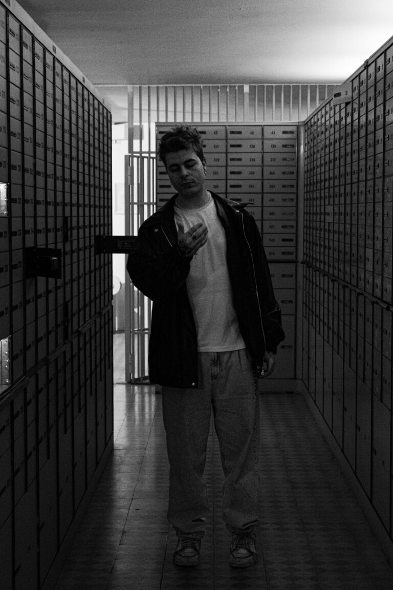 Man standing in a bank vault, surrounded by safety deposit boxes in black and white.